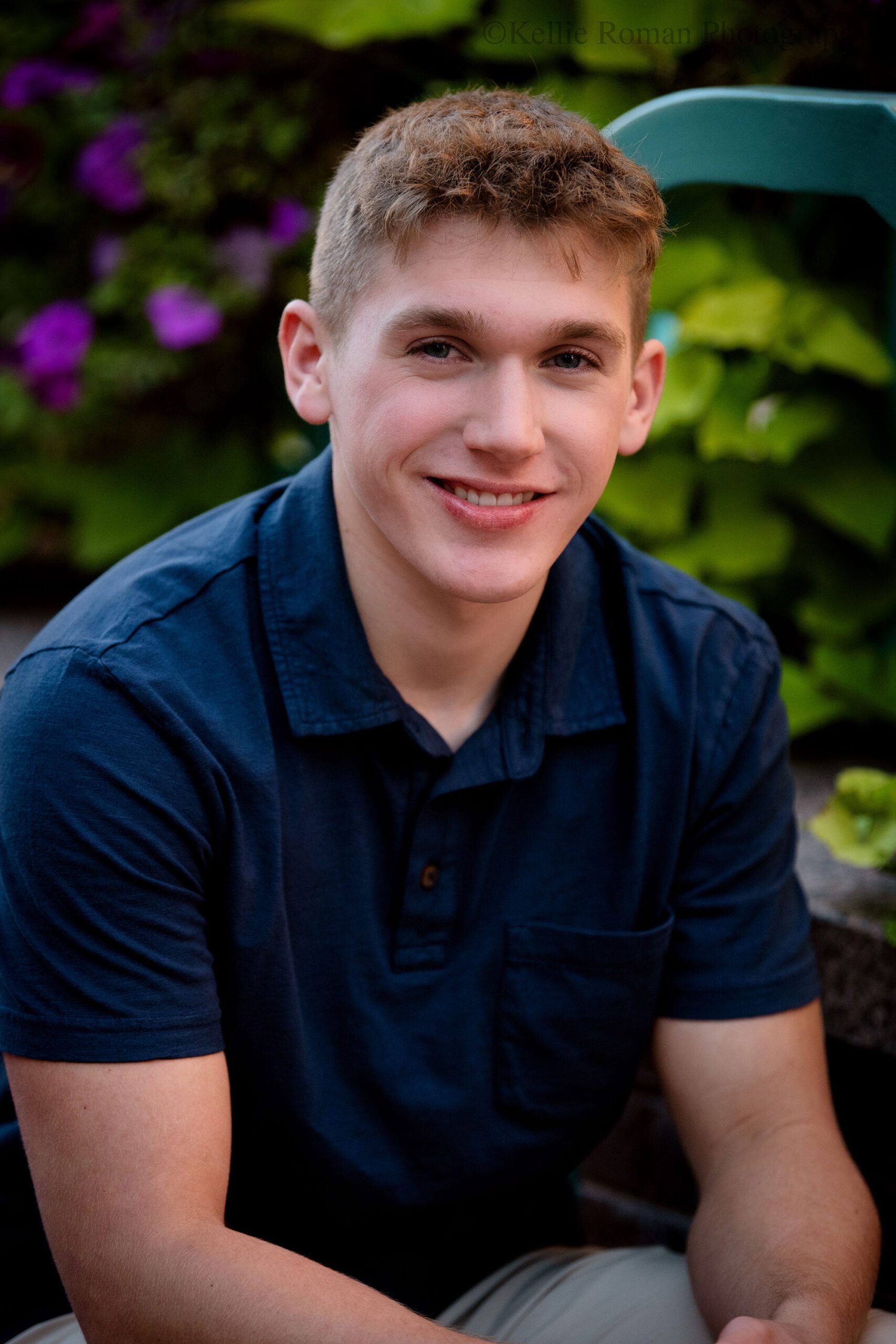 senior session in milwaukee. high school senior from Greendale is sitting in front of green and purple flowers in Downtown Milwaukee. it's a headshot, and the senior has a navy blue polo shirt on. 