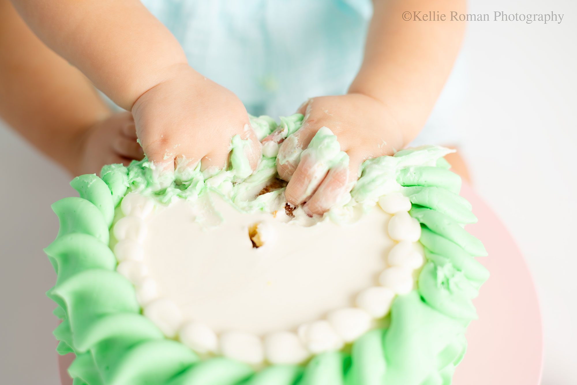 milwaukee pastel cake smash. close up shot of a one year old girl shoving her hands into a green and white cake. 