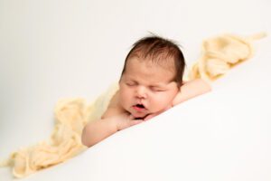 bright colored newborn photography. baby boy is asleep on his belly with his hands under his chin. he's on top of a white fabric, with a yellow fabric covering his diaper.