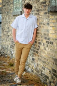 milwaukee senior pictures Franklin senior. high school senior guy leaning against old brick cobblestone building. he's wearing khakis and a blue dress shirt and has his hands in his pockets.
