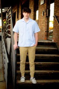 milwaukee senior pictures Franklin senior. high school senior guy is standing on old dirty stairs in milwaukee downtown. he's holding onto a metal railing. he's wearing khakis and blue dress shirt.