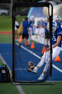 oak creek high school photographer. image of the oak creek football team warming up while kicking the ball into a net on the sidelines during the game.