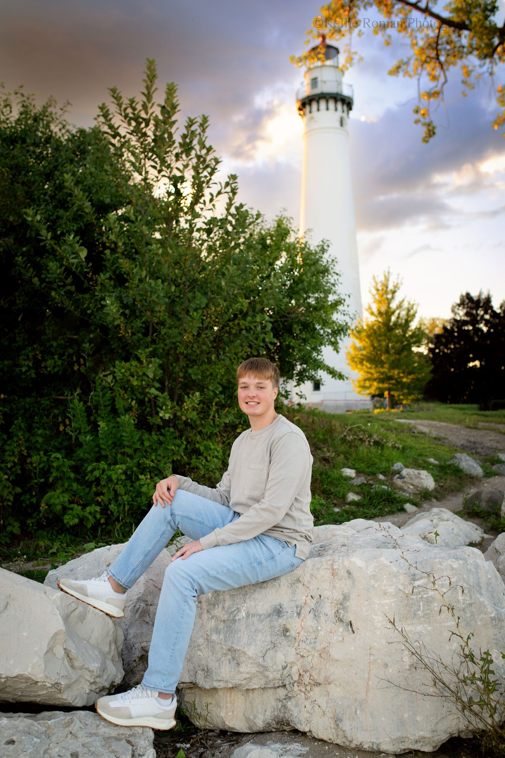 milwaukee senior photos. Muskegon high school senior sitting on large rocks in front of white lighthouse in racine.