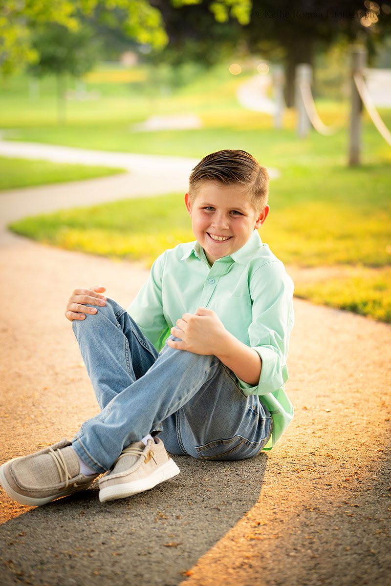 birthday photo session. ten year old boy sitting on paved bath with sun setting behind him.