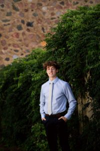kettle moraine senior photographer. high school senior guy standing in front of ivy wall. he has on blue dress pants a blue dress shirt and grey tie. he has his hands in his pockets.