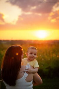milwaukee family photographer. a mother is holding her baby boy in a milwaukee park. the boy is looking at the camera, and the glow of the sunset is behind them.