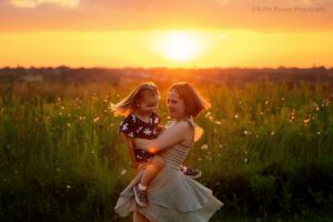 milwaukee family photographer. a girl is holding her baby brother and twirling around with him in milwaukee park. the sun is setting behind them and it's glowing orange.